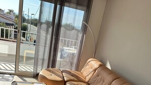 A modern living room with a brown leather sofa, a glass-top coffee table, and a view of the street through large windows.