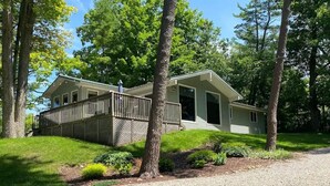 A single-story house with a front deck, surrounded by trees and a well-maintained lawn. - Beautiful 3 bedroom, 1 bath cottage in the heart of Port Franks, Ontario.  (Port Franks)