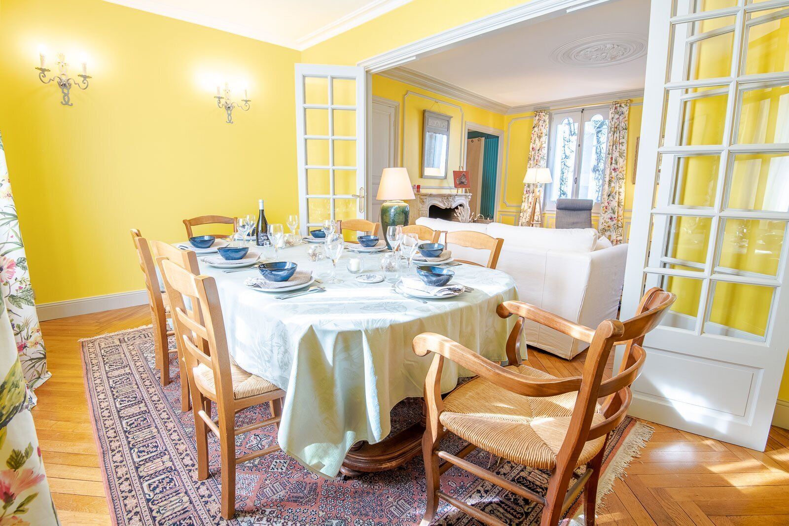 Uma sala de jantar com uma mesa redonda posta para seis pessoas, rodeada por cadeiras de madeira.