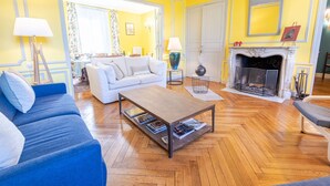 A living room with a fireplace, a sofa, a coffee table, and a dining area in the background. - Le Clos des Tilleuls - Gite 10 people (Francueil)