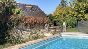 A swimming pool with a stone wall and a thatched roof structure in the background. - Le Clos des Tilleuls - Gite 10 people (Francueil)