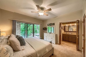 A bedroom with a large bed, a dresser, a vanity with a mirror, and a ceiling fan.