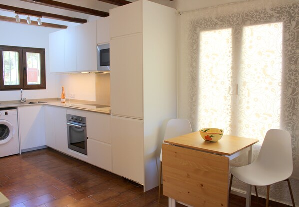 A compact kitchen with a washing machine, oven, and a dining area with a table and chairs. - Moraira, Lovely Apartment in Beautiful Complex with Communal Pool (Moraira)