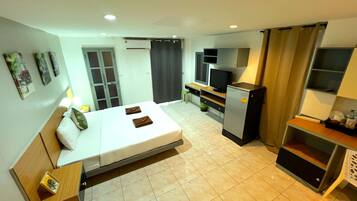 A hotel room with a bed, a desk with a computer, a TV, and an air conditioning unit.