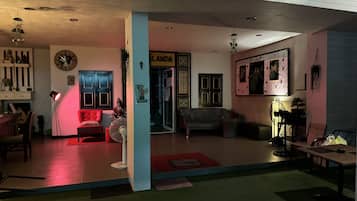 A spacious living area with a red sofa, a black leather couch, and a dining table. A large clock and a framed picture adorn the walls.