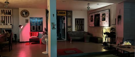 A spacious living area with a red sofa, a black leather couch, and a dining table. A large clock and a framed picture adorn the walls.