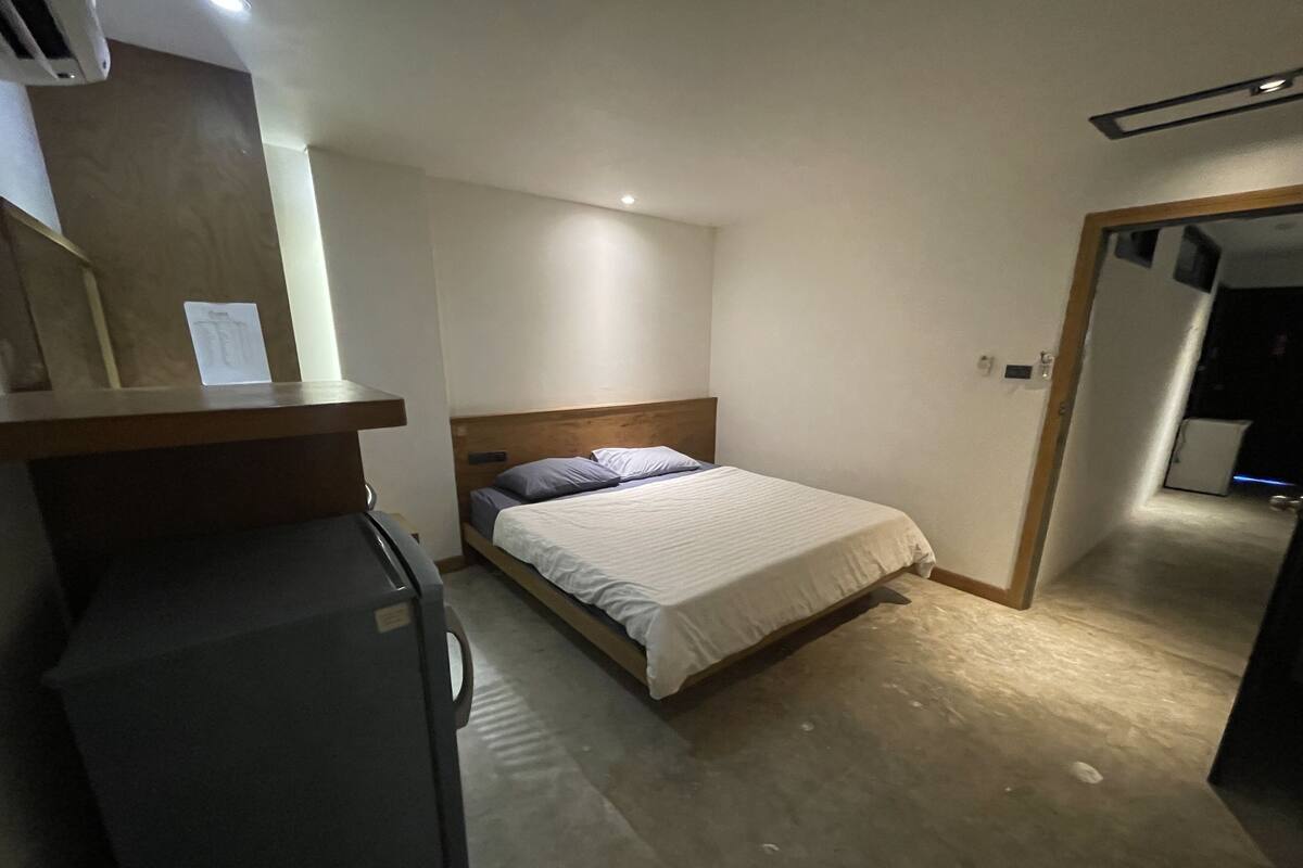Ein kleiner, kompakter Raum mit einem Einzelbett, einem Schreibtisch und einem Kühlschrank.