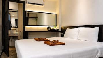 A hotel room with a bed, a bedside table, a mirror, an air conditioning unit, and a bathroom visible through an open door.