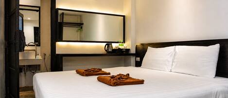 Habitación de hotel con cama, mesita de noche, espejo, unidad de aire acondicionado y baño visible a través de una puerta abierta.
