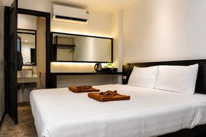 A hotel room with a bed, a bedside table, a mirror, an air conditioning unit, and a bathroom visible through an open door. - Cocoon Islanda Hotel (Patong)