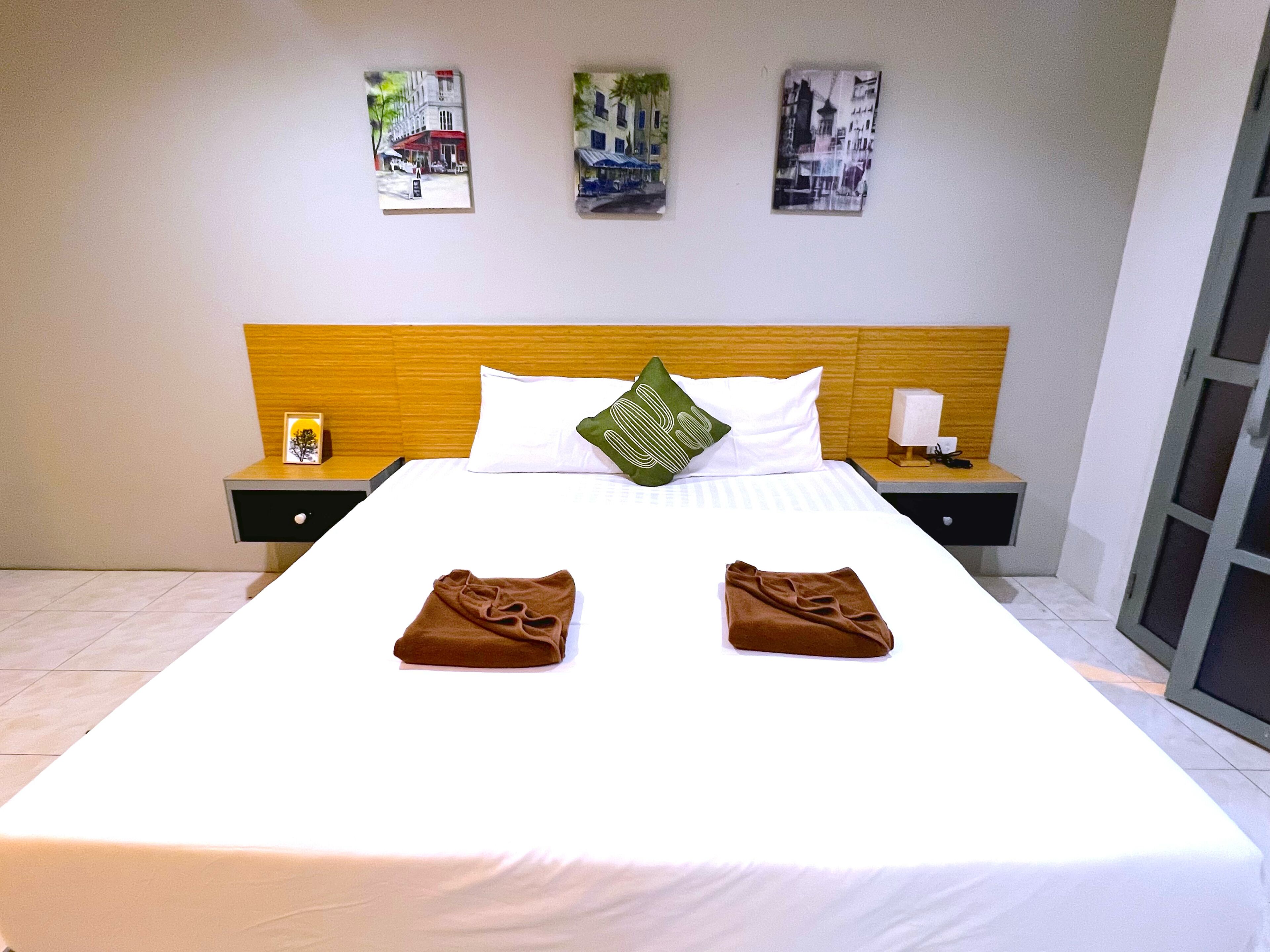 A hotel room with a large bed, two pillows, a nightstand with a lamp, and three wall art pieces.