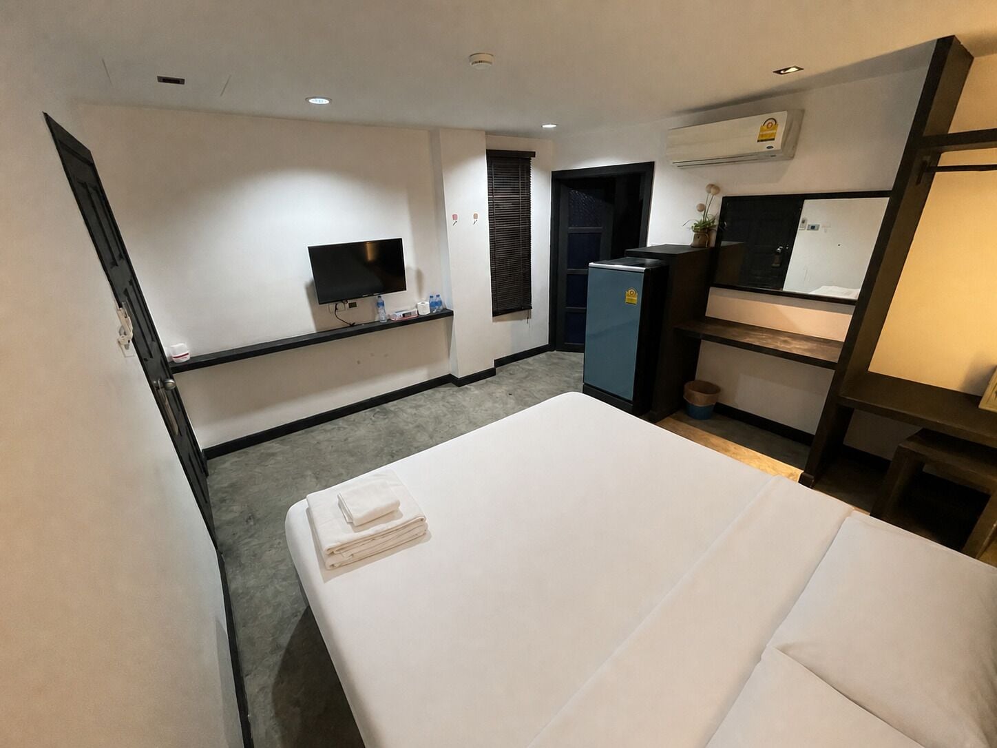 A hotel room with a bed, a television, a minibar, and a desk with a computer.