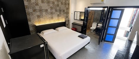 A hotel room with a bed, a desk, a wardrobe, a bathroom, and a view of the outside.