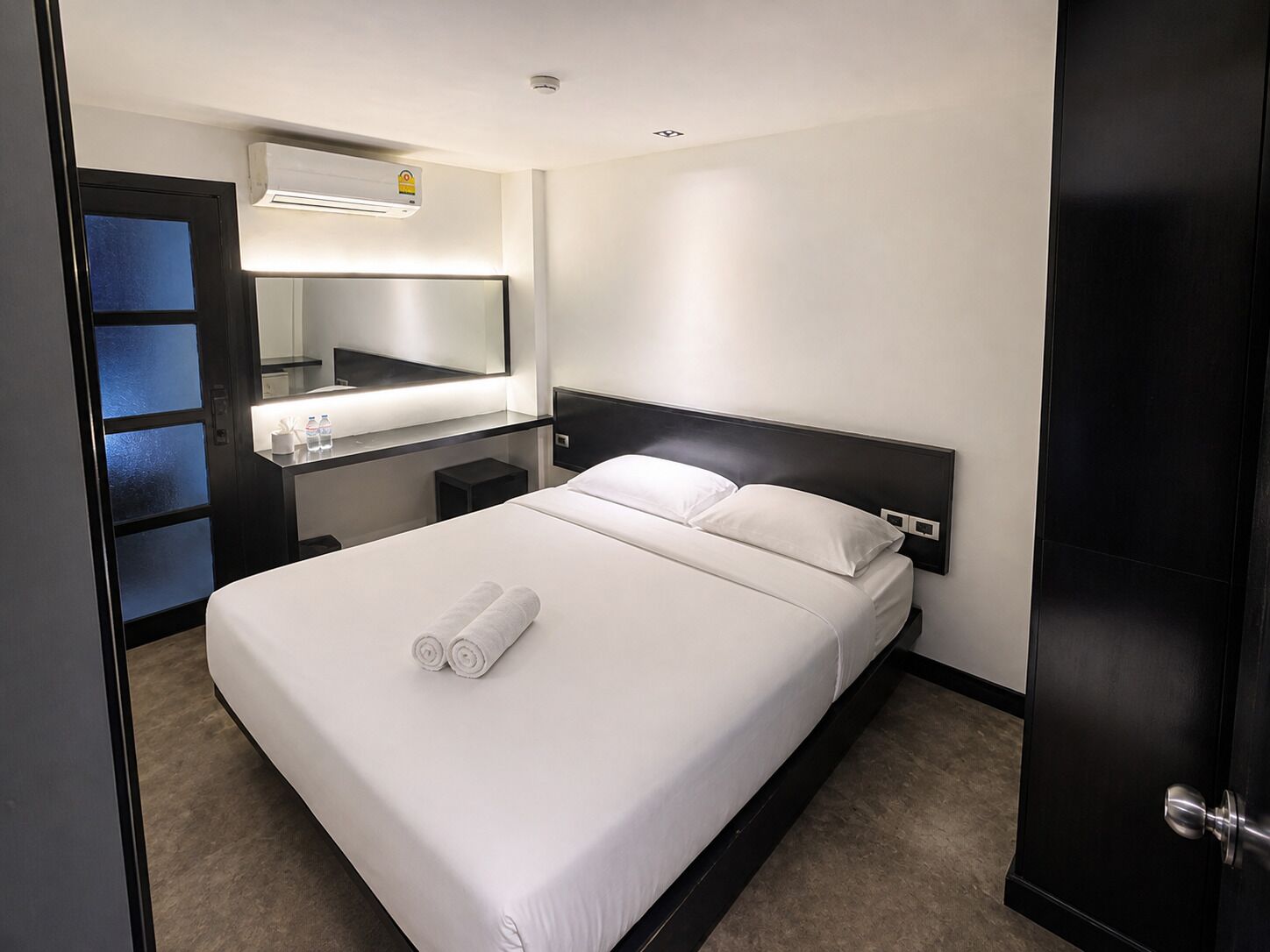 Une chambre d’hôtel équipée d’un lit, d’une table de chevet, d’un miroir et d’un climatiseur fixé au mur.