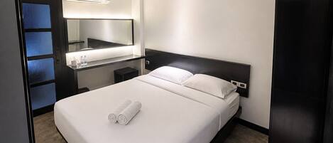 A hotel room with a bed, a bedside table, a mirror, and a wall-mounted air conditioning unit.