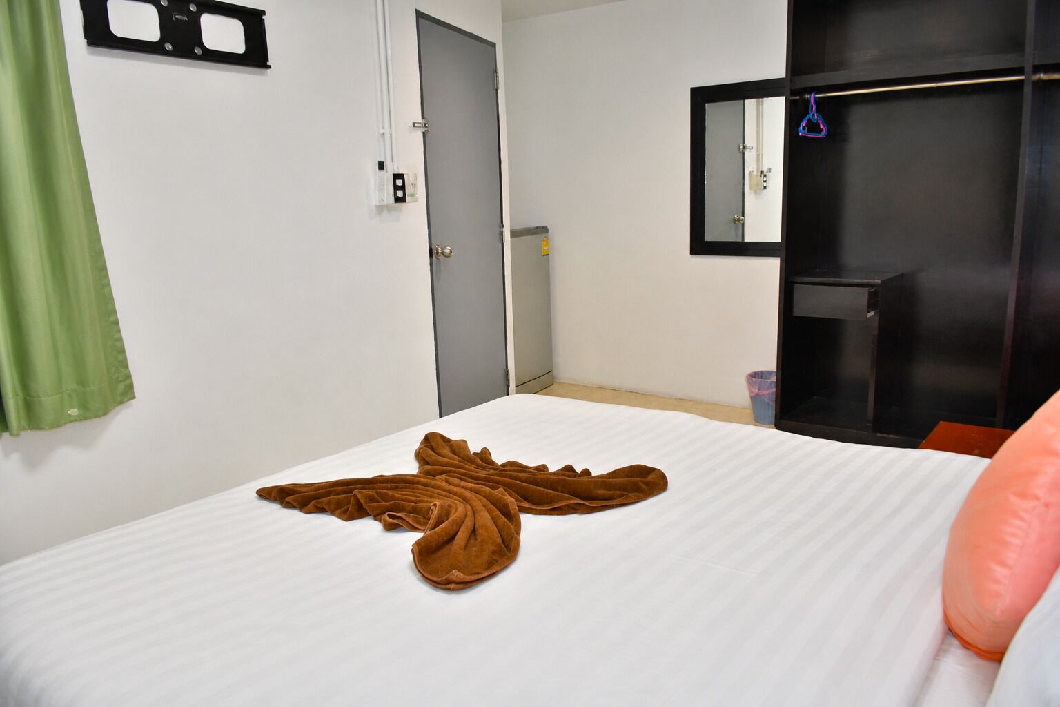 Quarto de hotel com uma cama, cortina verde, porta, espelho e guarda-roupa preto.