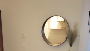 A room with a round mirror on the wall, a wooden console table with a vase, and a black metal frame.