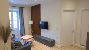A modern living room with a sofa, a coffee table, a TV mounted on the wall, and a wooden floor.