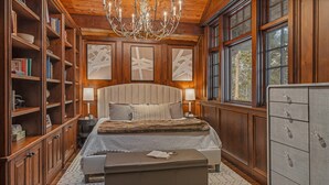 Une chambre avec un grand lit, des étagères en bois, un lustre et une vue par la fenêtre.