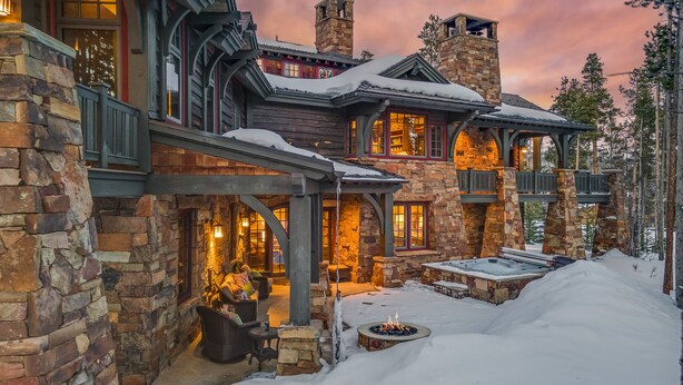 Un bâtiment en pierre doté d’une cheminée, d’un espace extérieur aménagé pour s’asseoir et d’une terrasse recouverte de neige.