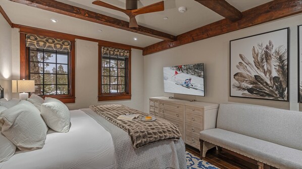 A bedroom with a bed, a TV, a sofa, and a large window with a view of trees.