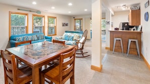 A cozy living area with a blue sofa, a wooden dining table, and a kitchen area with stools.
