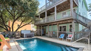 A pool area with a wooden deck, lounge chairs, and a staircase leading to a balcony.