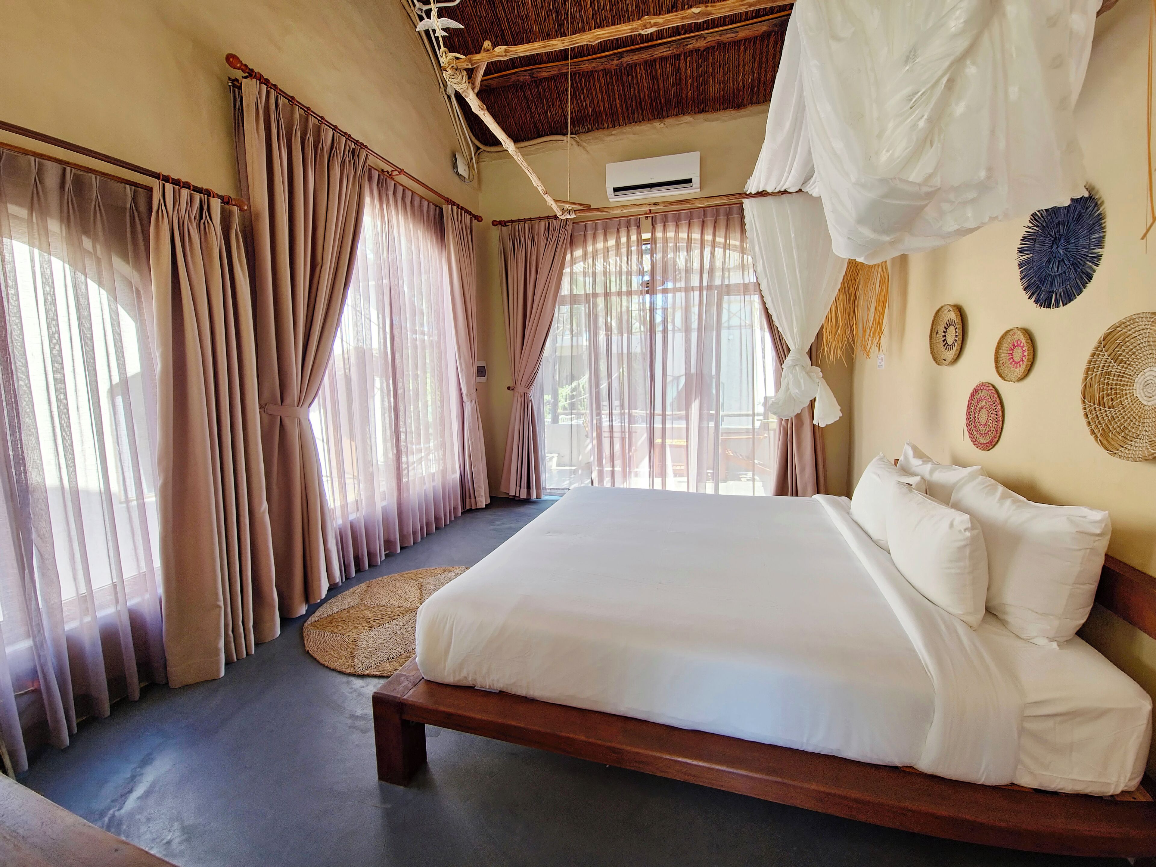 A bedroom with a wooden bed, beige curtains, a woven mat, and a ceiling fan.