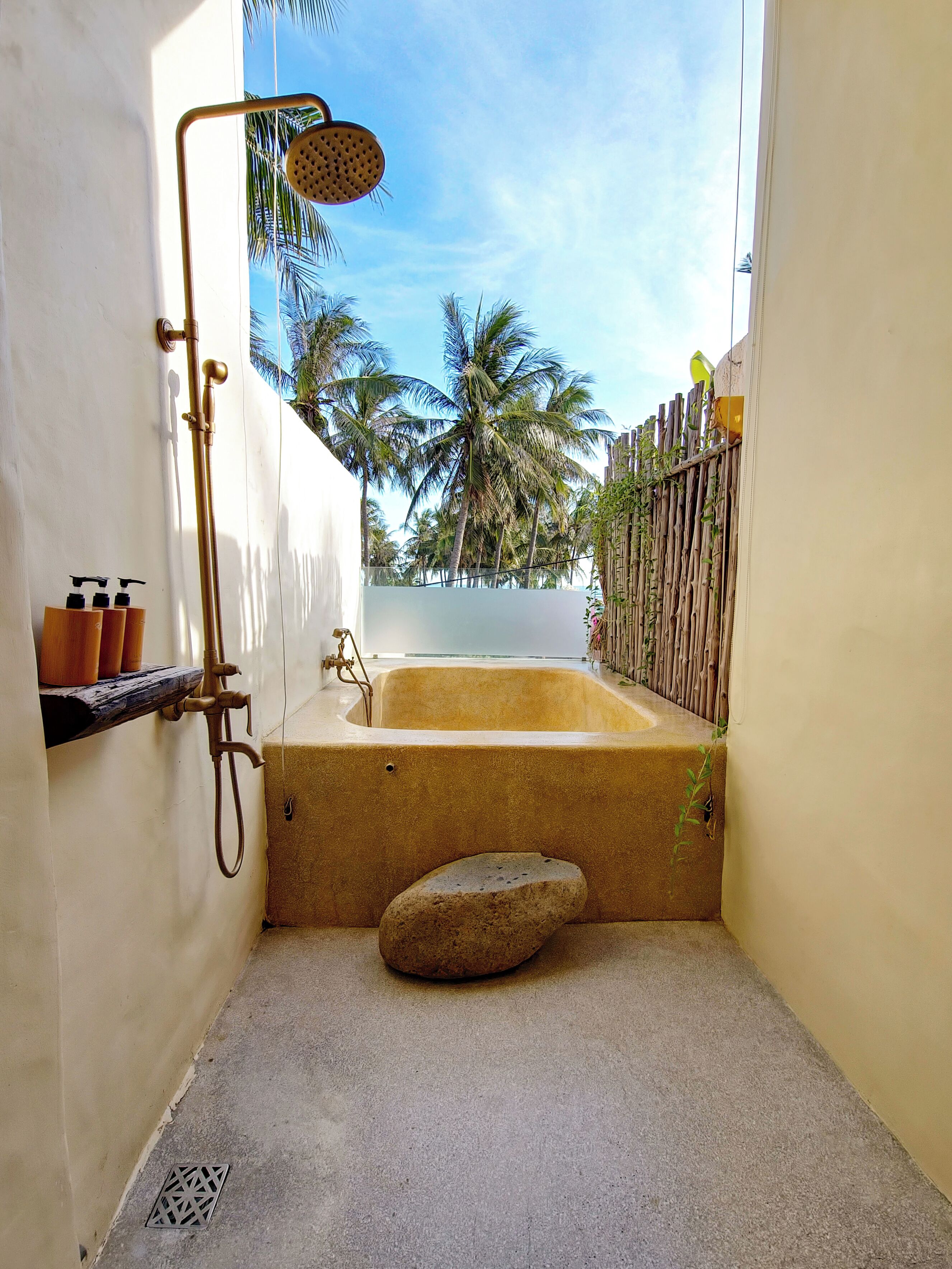 A small, enclosed bathroom with a bathtub, shower, and a stone seating area.