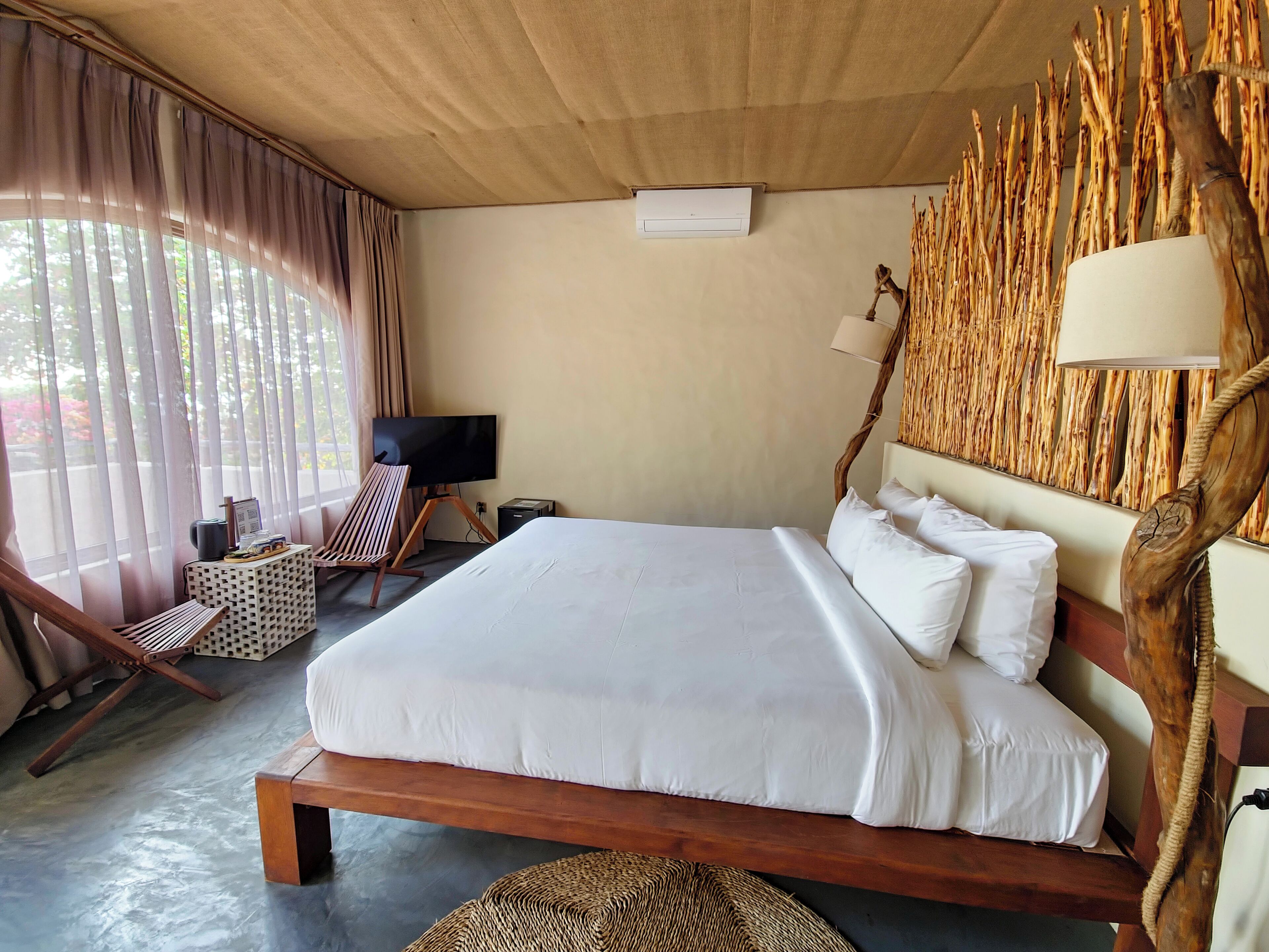 A bedroom with a large bed, a television, a wooden chair, and a wall-mounted lamp.