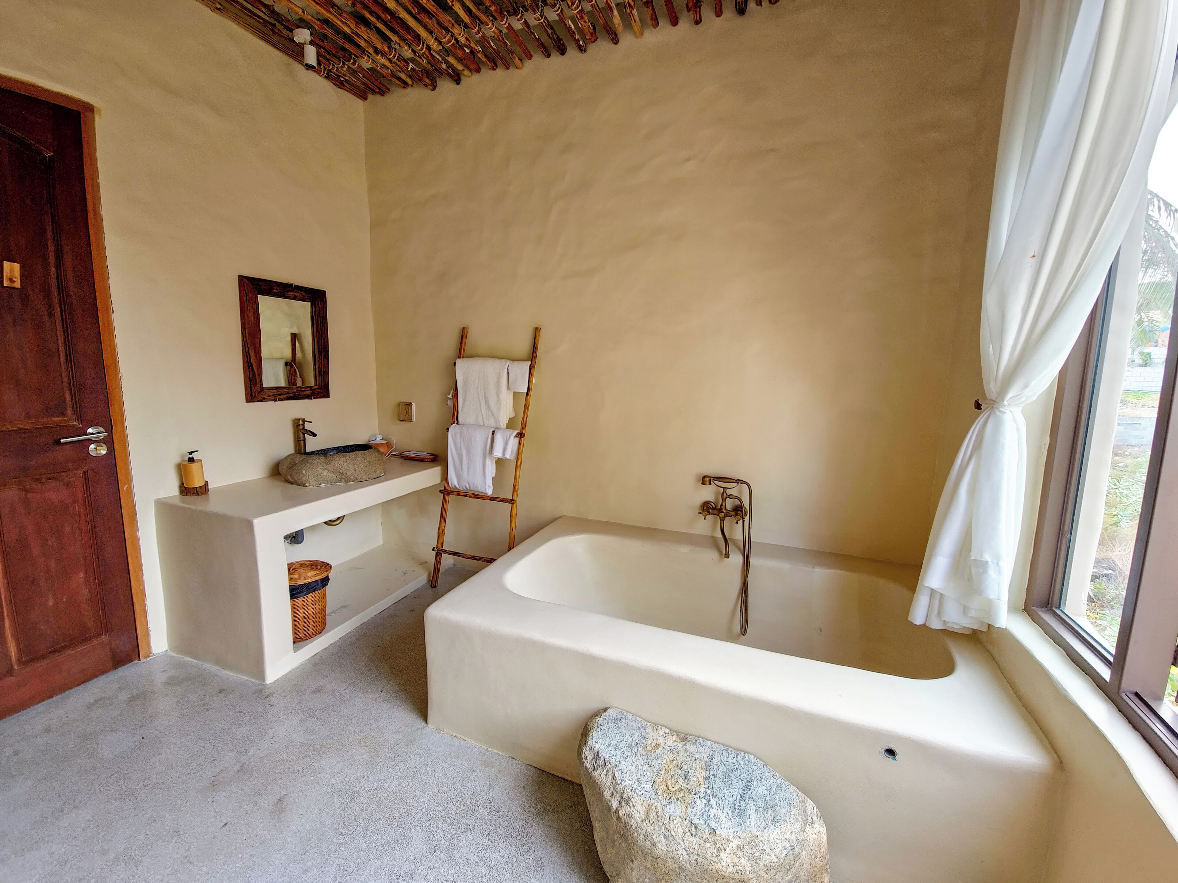 A bathroom with a bathtub, a wooden ladder, a sink, and a mirror.