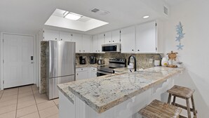 Una cocina moderna con armarios blancos, encimera de granito, electrodomésticos de acero inoxidable y tragaluz.