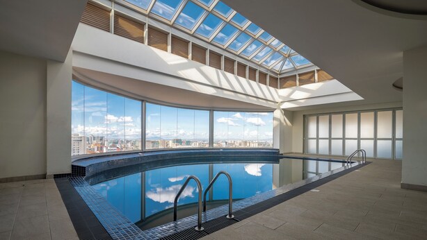 Uma grande piscina interior com claraboia, vista da cidade e design moderno.