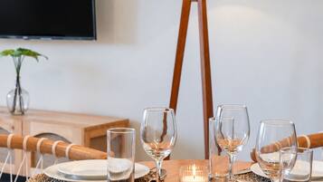 A dining table set with plates, glasses, and a candle, with a lamp and TV in the background.