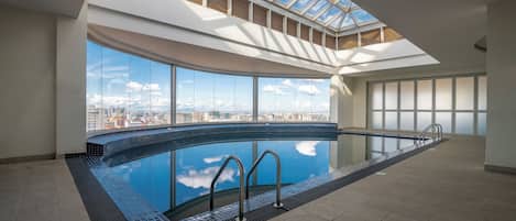 A large indoor swimming pool with a city view, skylight, and modern architecture.