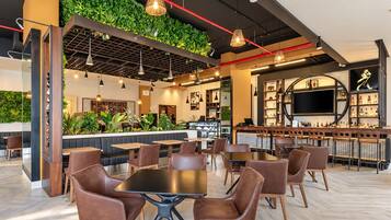 Ein modernes Restaurant mit Barbereich, Holztischen und Pflanzen an der Decke.