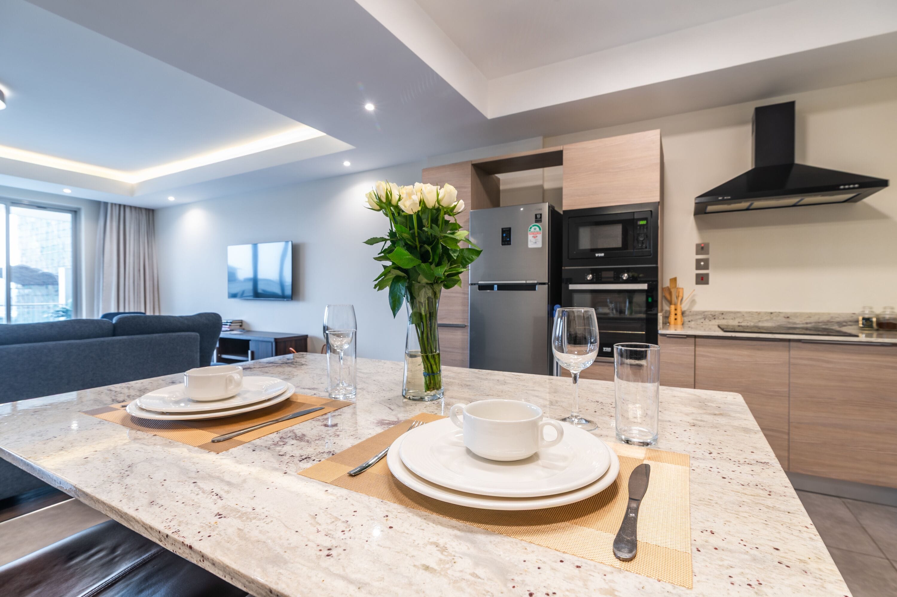 Una cocina moderna con una isla central, electrodomésticos integrados y un comedor con una mesa dispuesta para dos personas.