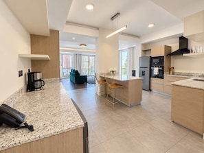 Una cocina moderna con una isla central, electrodomésticos integrados y una zona de estar con sofá y sillas.