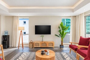 A hotel room with a flat-screen TV, a wooden console table, a red sofa, a coffee table, a water dispenser, a lamp, and a large plant. - Capital M Apartments by YourHost (Nairobi)