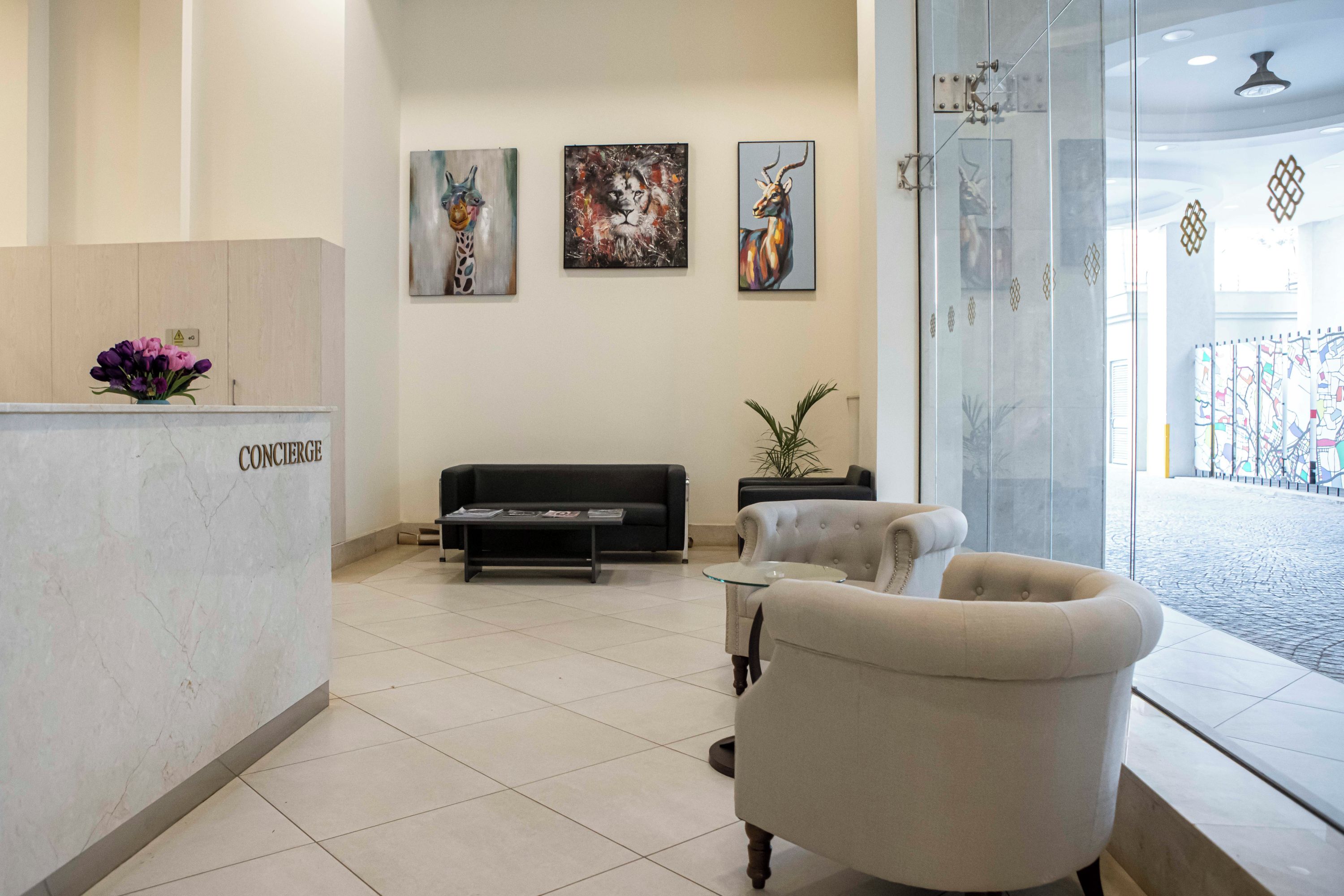 A reception area with a reception desk labeled 'CONCIERGE,' a black sofa, a small table, and three wall-mounted paintings.