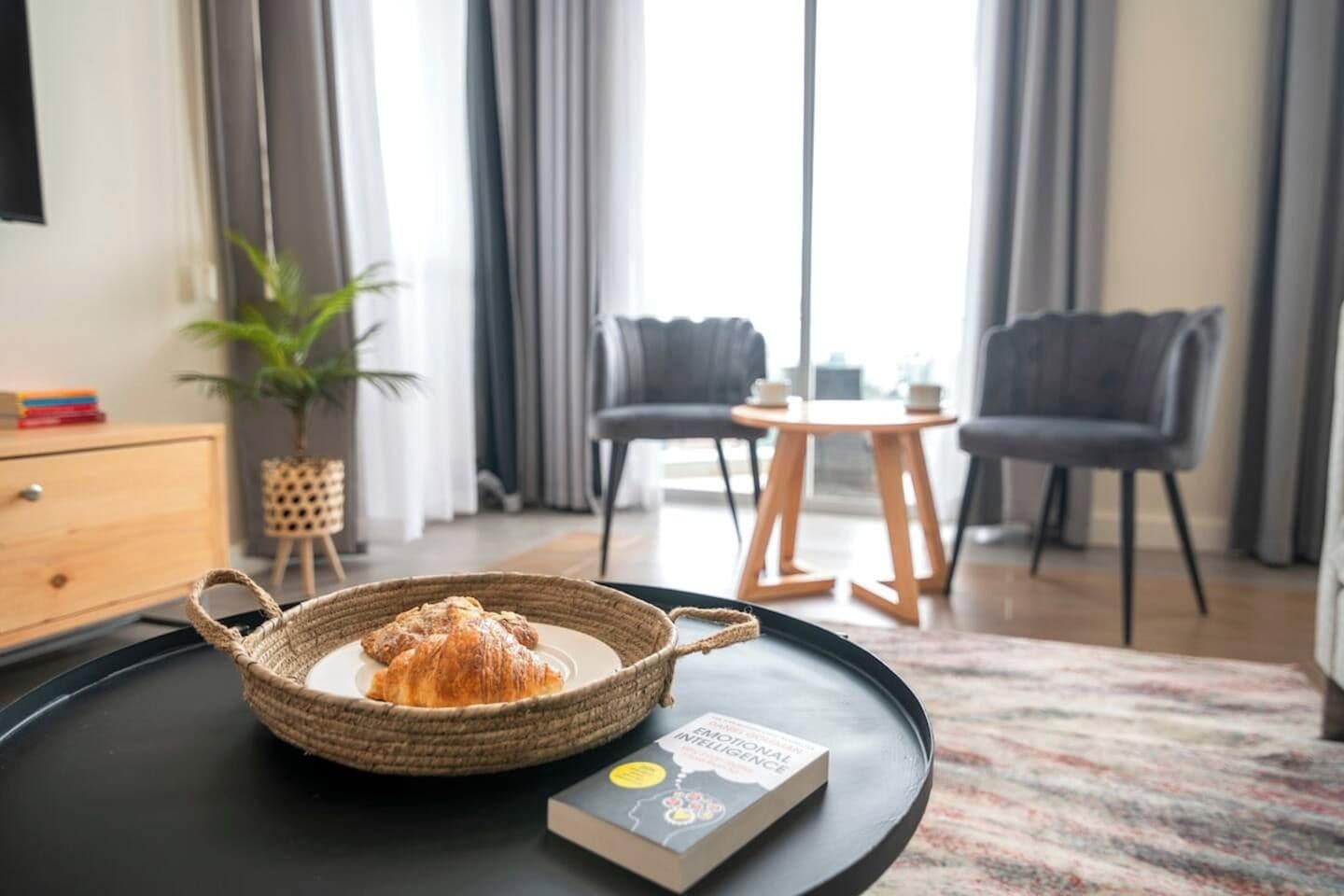 A cozy room with a dining area, a bookshelf, and a window with curtains.