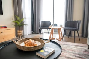 A cozy room with a dining area, a bookshelf, and a window with curtains. - Capital M Apartments by YourHost (Nairobi)