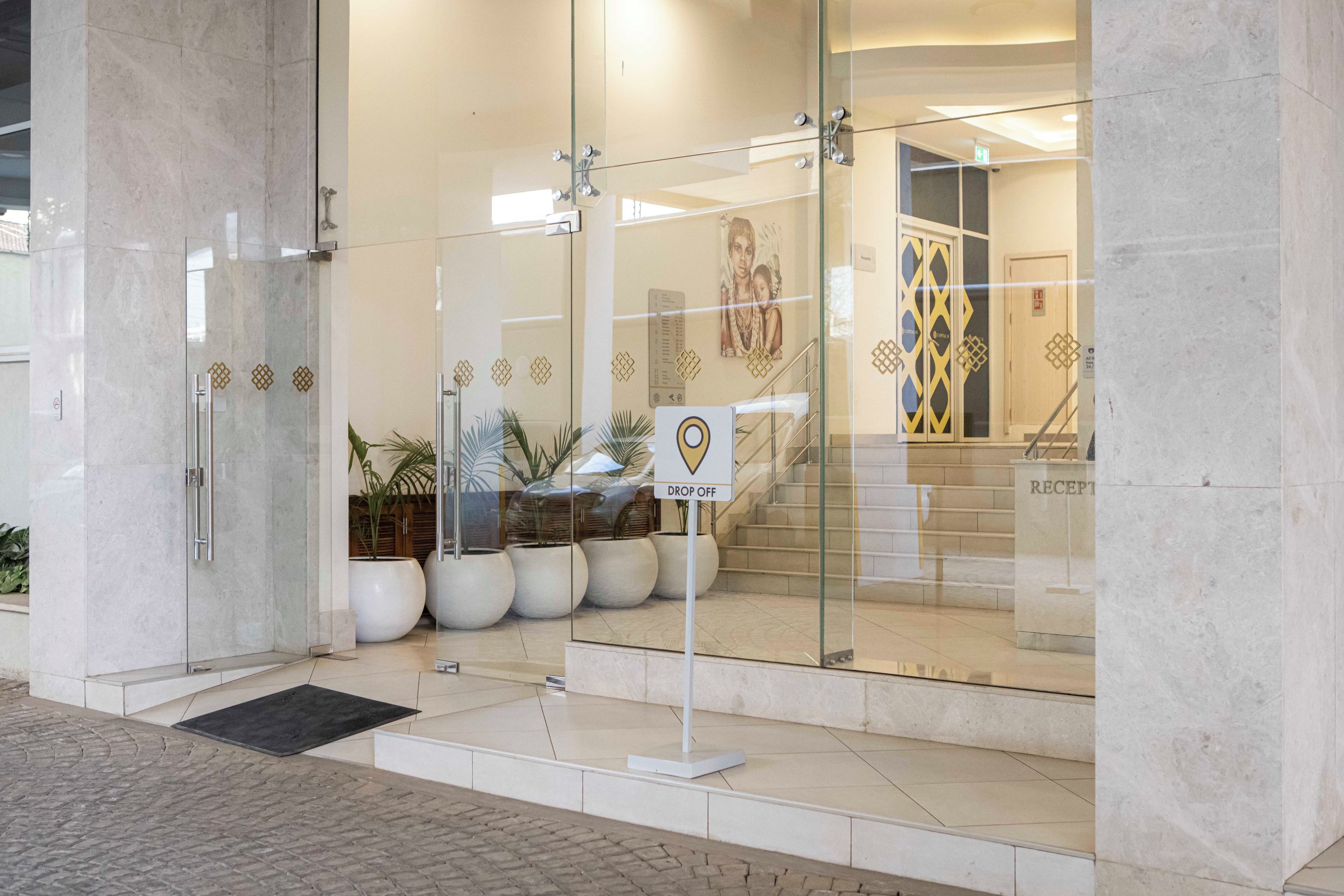 Entrada de hotel com porta de vidro, balcão de recepção e escada que leva para dentro.