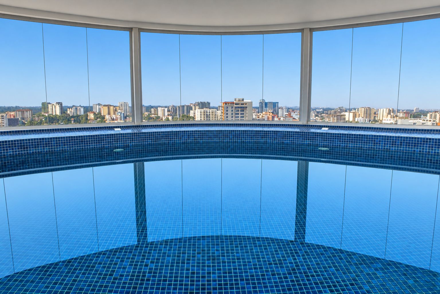 A large indoor swimming pool with a cityscape view through large windows.