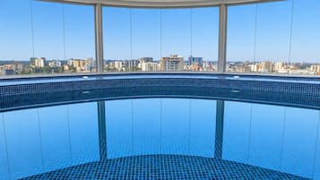 En stor indendørs swimmingpool med udsigt over bybilledet gennem store vinduer.