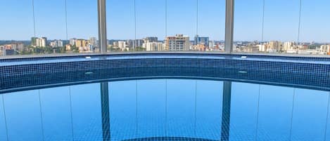 A large indoor swimming pool with a cityscape view through large windows.