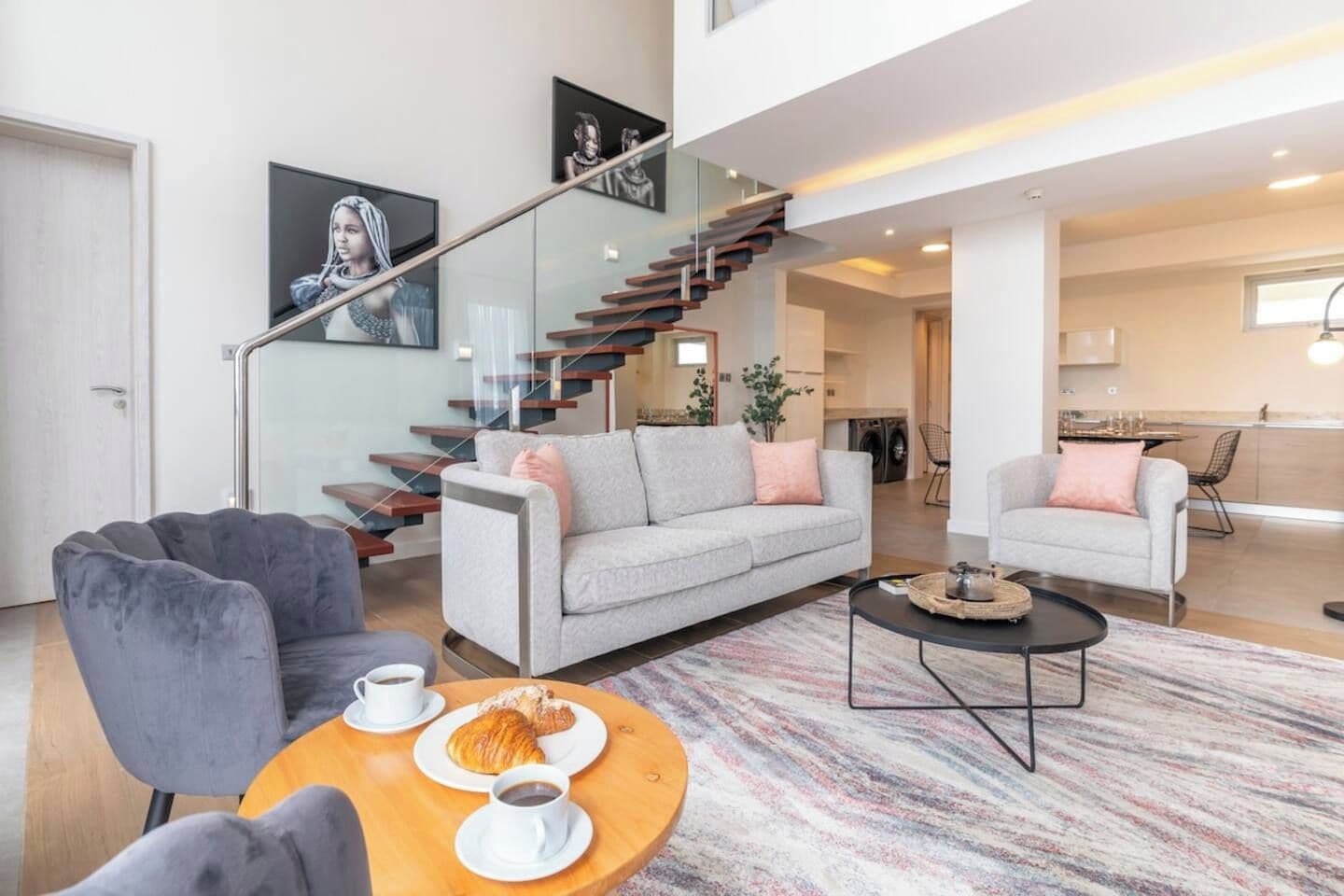 A modern living room with a sofa, armchairs, a coffee table, and a staircase.