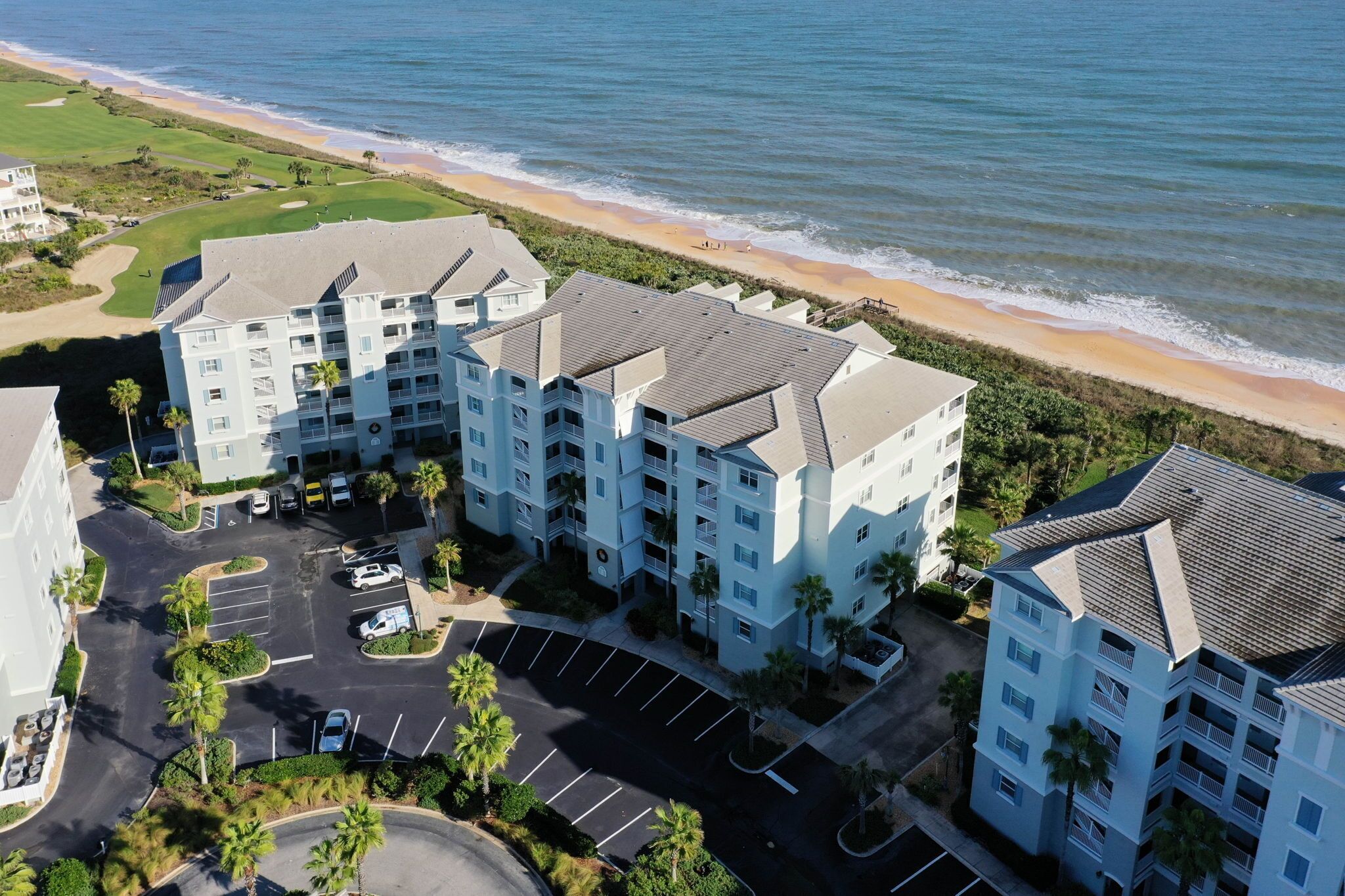 A multi-story hotel with a parking lot and a view of the beach.