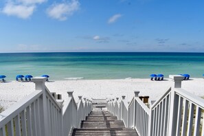 A wooden staircase leading to a beach with white railings and blue umbrellas.