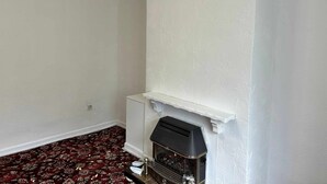 Una habitación con chimenea, papel tapiz estampado con motivos florales y alfombra roja.